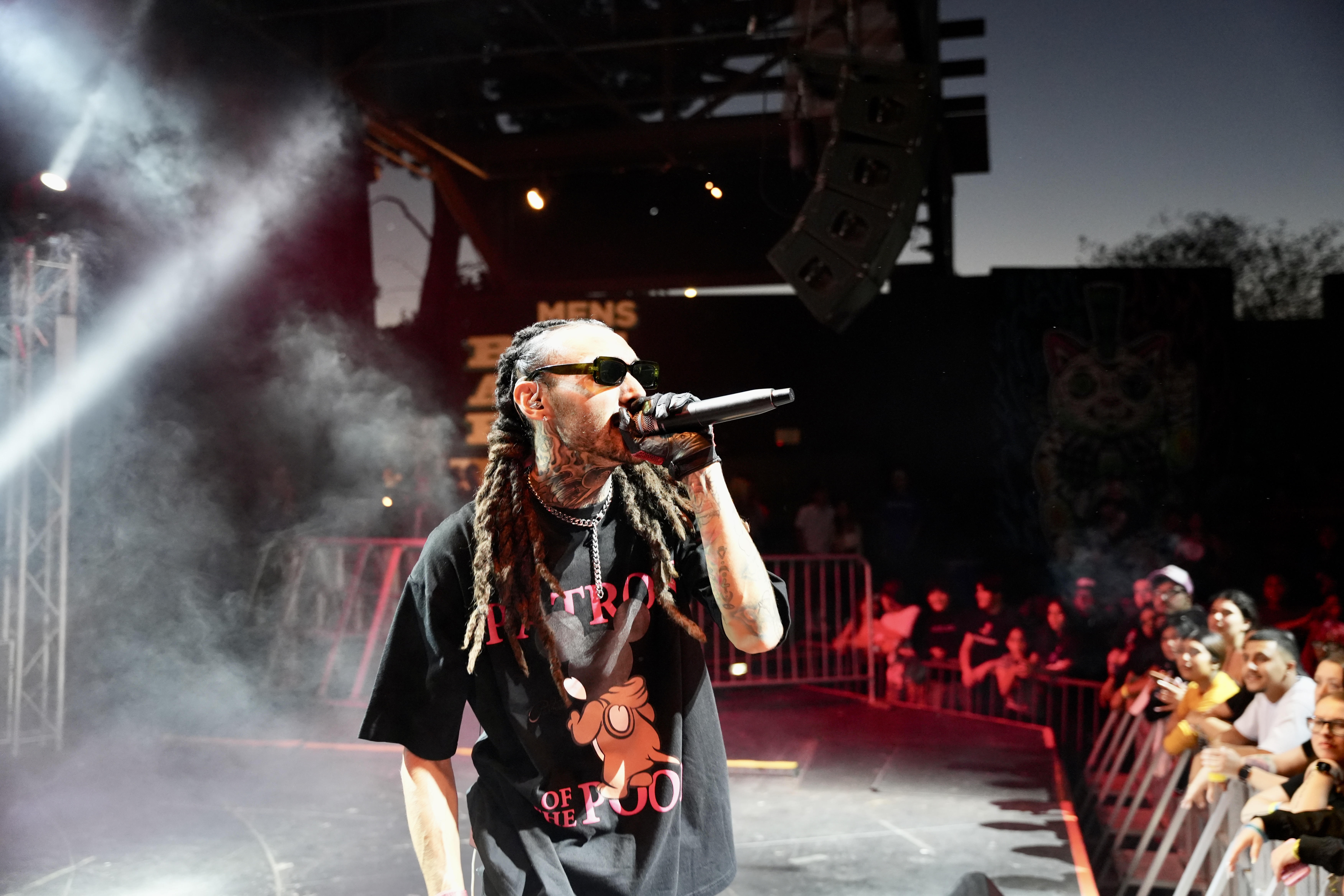 Kilohana singing into a microphone on stage at The Garden Amp with the crowd visible beside him
